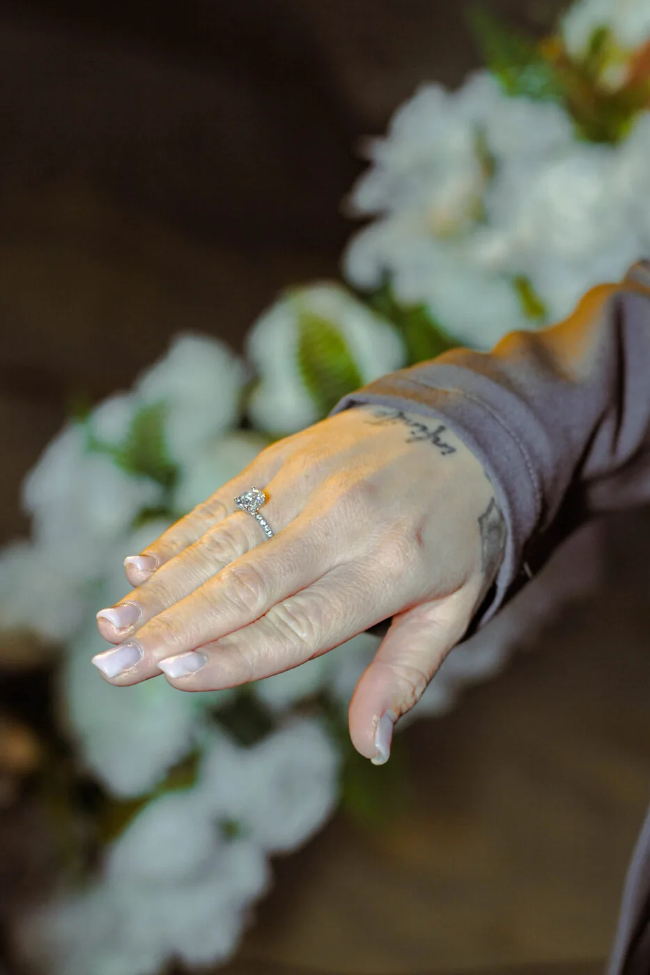 Hand met verlovingsring tussen witte bloemen